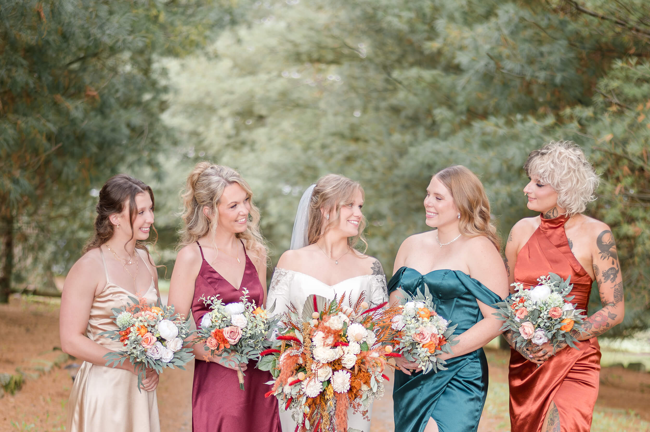 Bride smiling at her bridesmaids in front of the iconic pine trees at The Barn at Whispering Pines