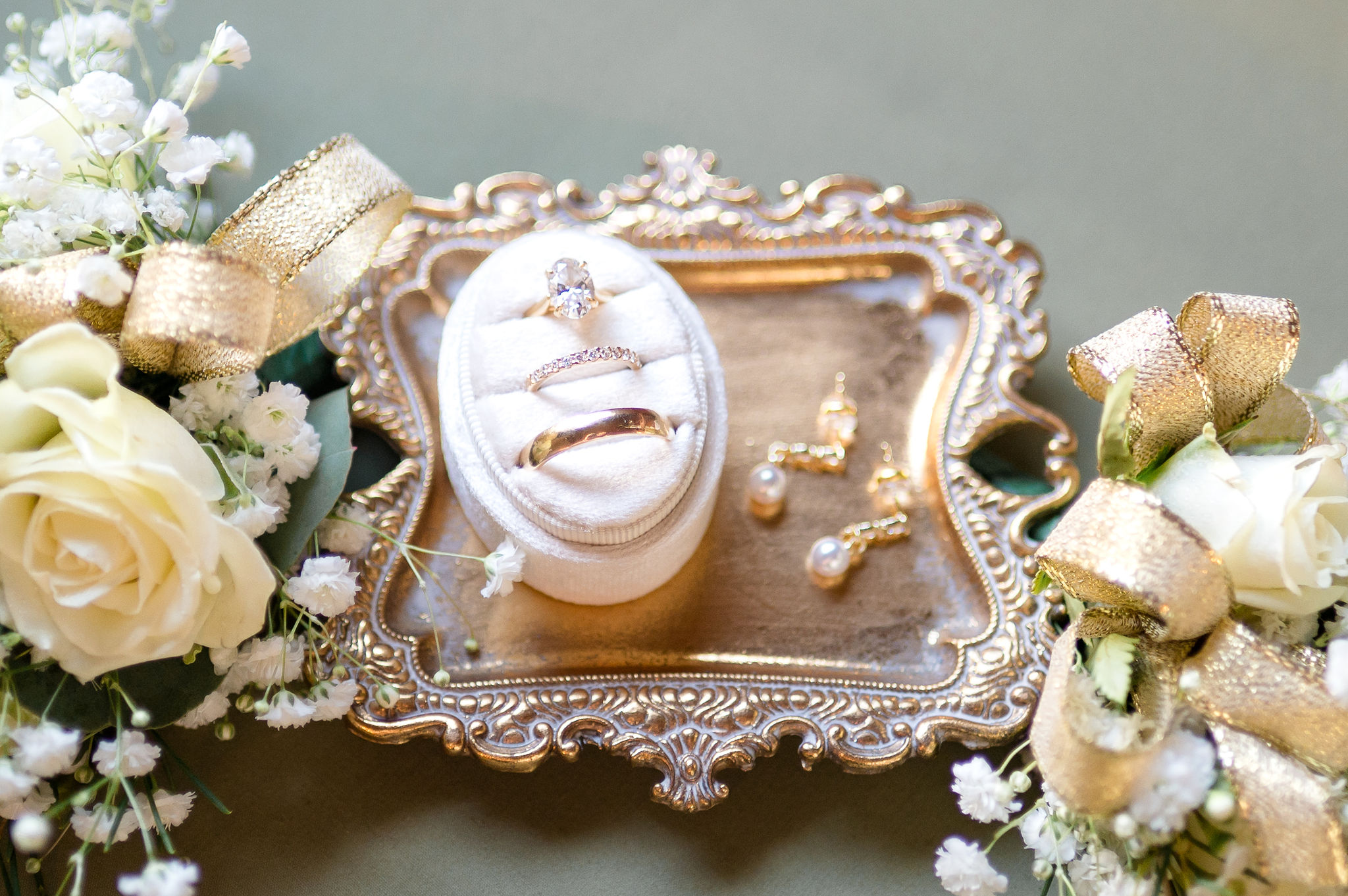 Bridal details of rings and pearl earrings on a gold tray with white roses