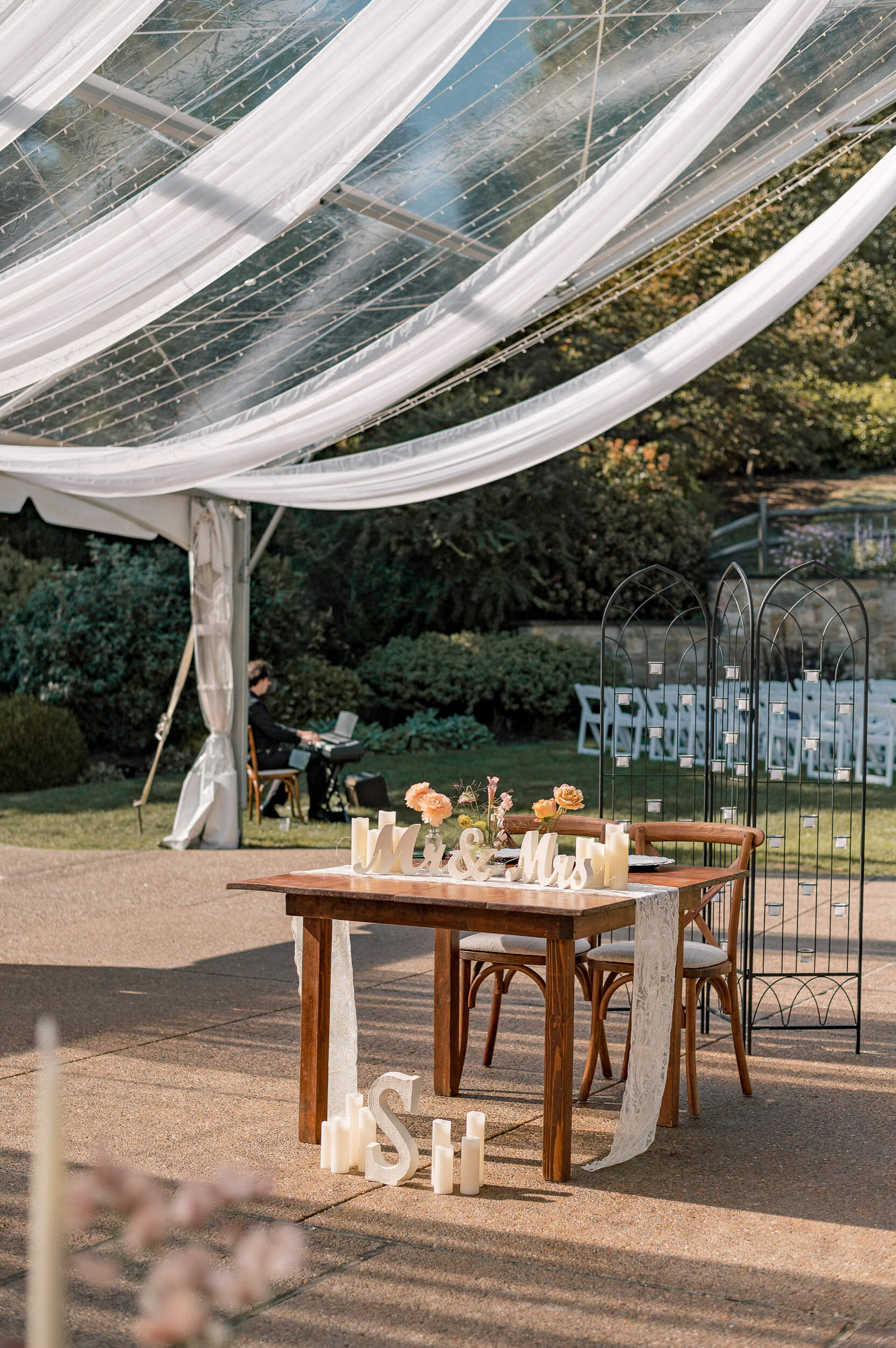 Details of a wooden head table for a reception under drapes and market lights of the lawn of one of the outdoor wedding venues in PA