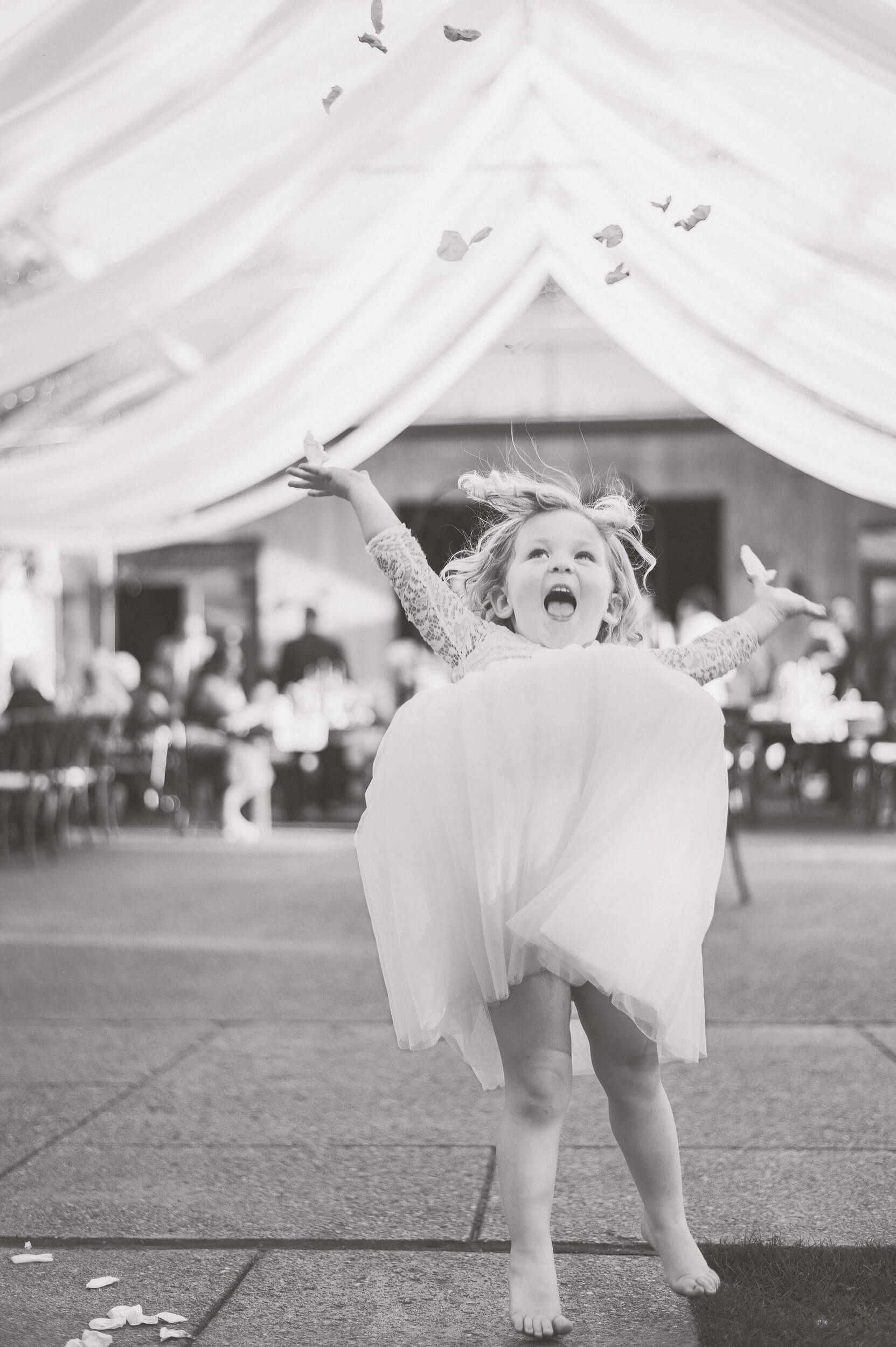 A toddler girl tosses flower petals in the air on the dance floor under a tent at one of the outdoor wedding venues in PA