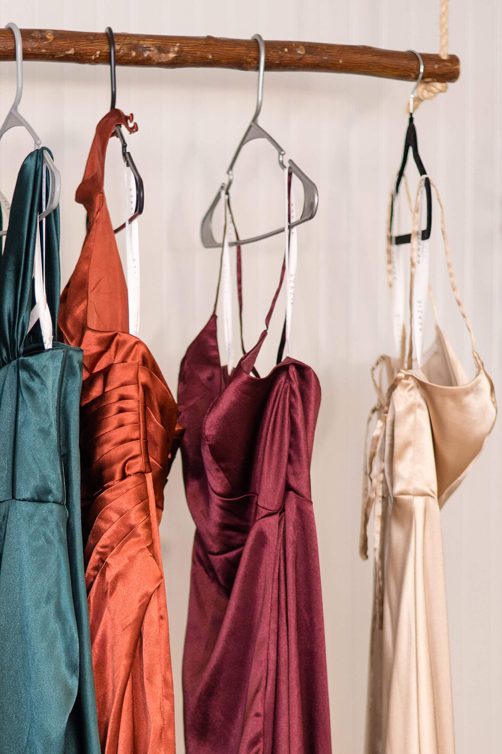 Details of a few bridesmaid dresses hanging on a wood rod in different colors