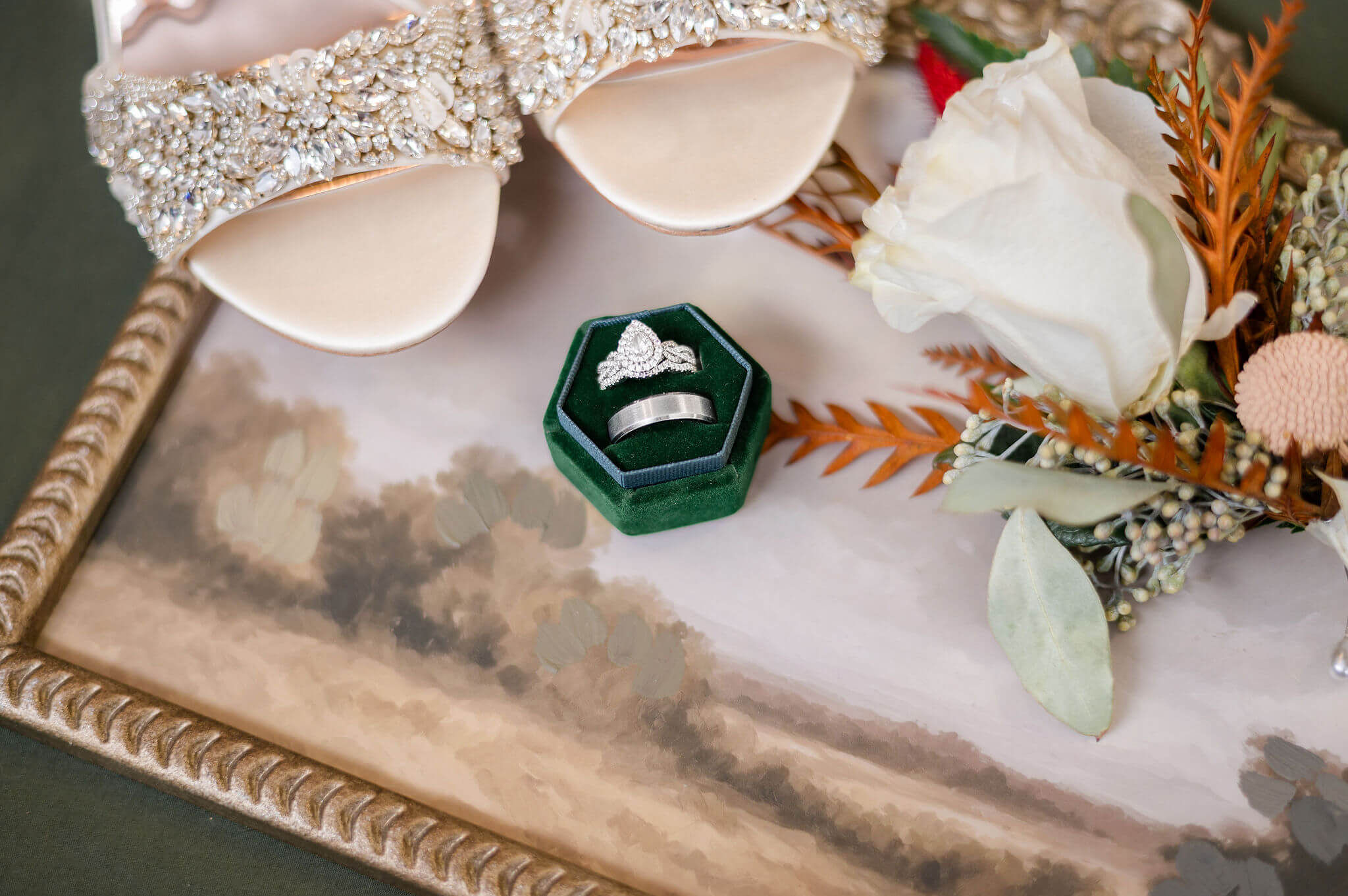 Details of a bride's shoes and rings on a painting with a white rose