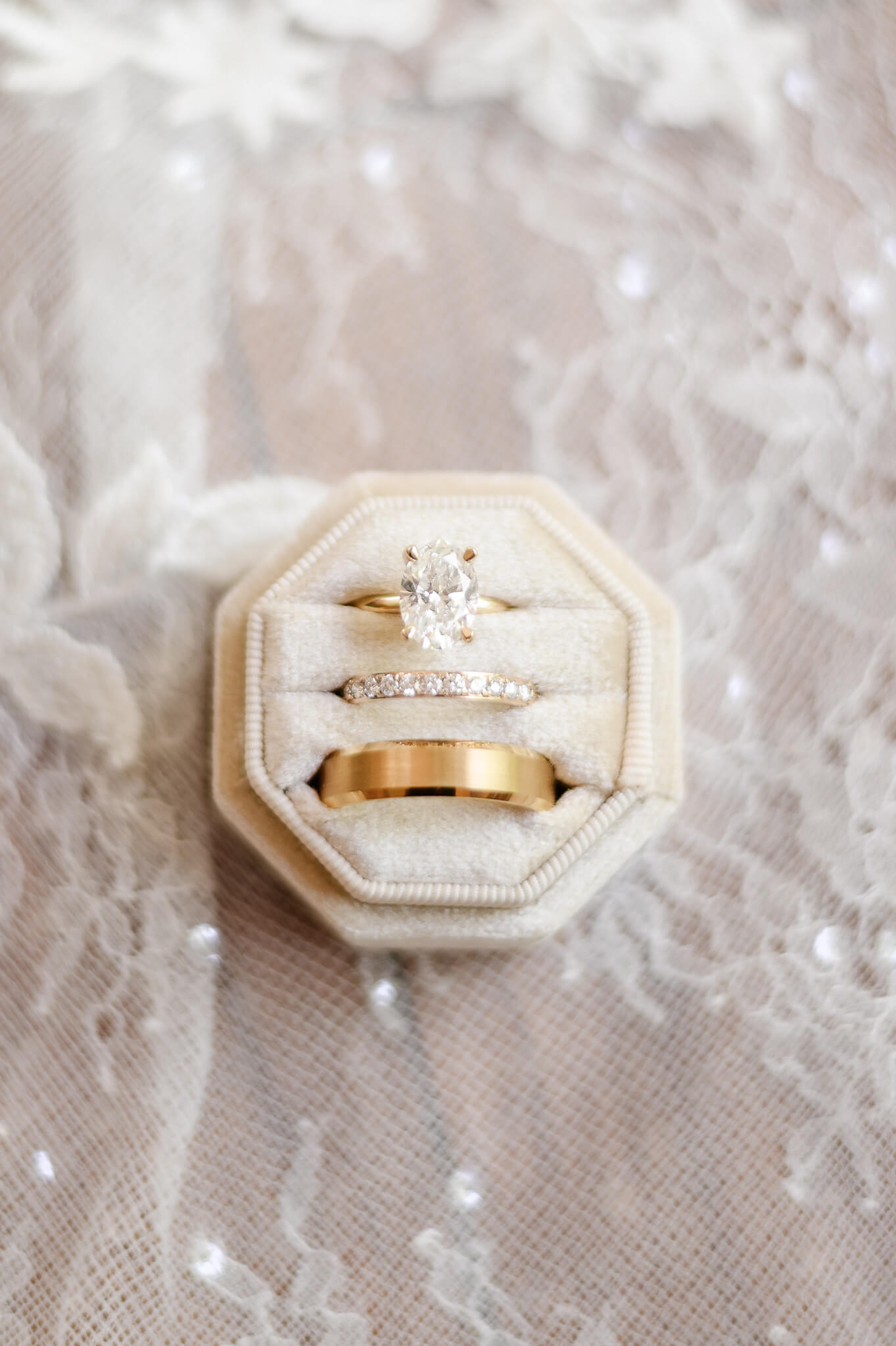 Gold oval diamond ring set pictured in a cream box on top of the train of the bridal dress.