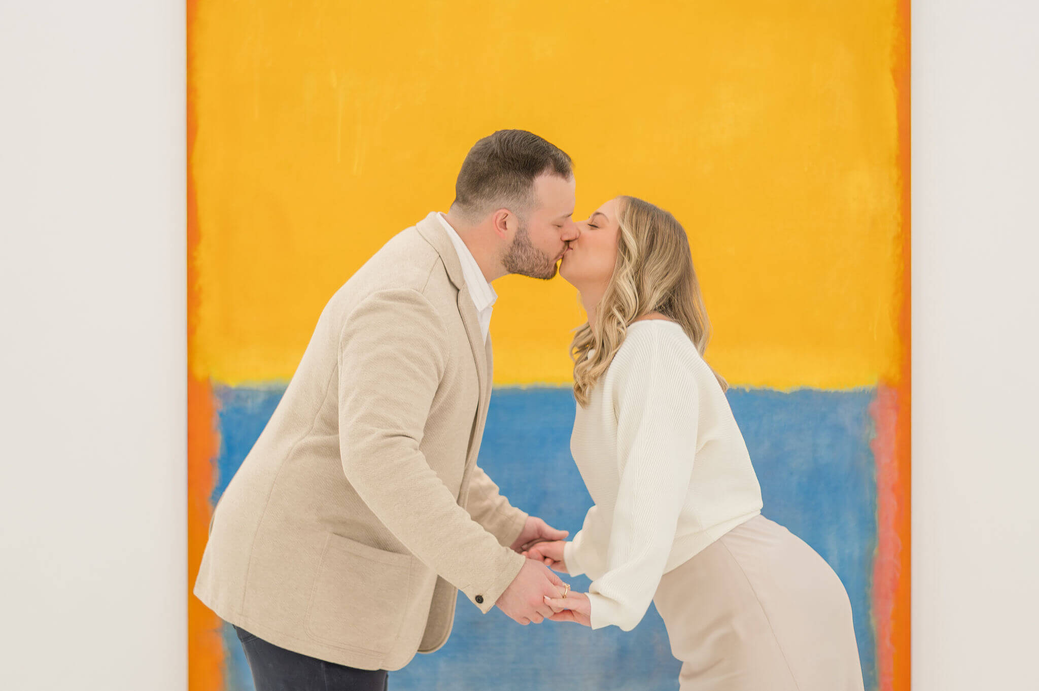 A couple kissing in front of a bright blue and yellow portrait at the art museum