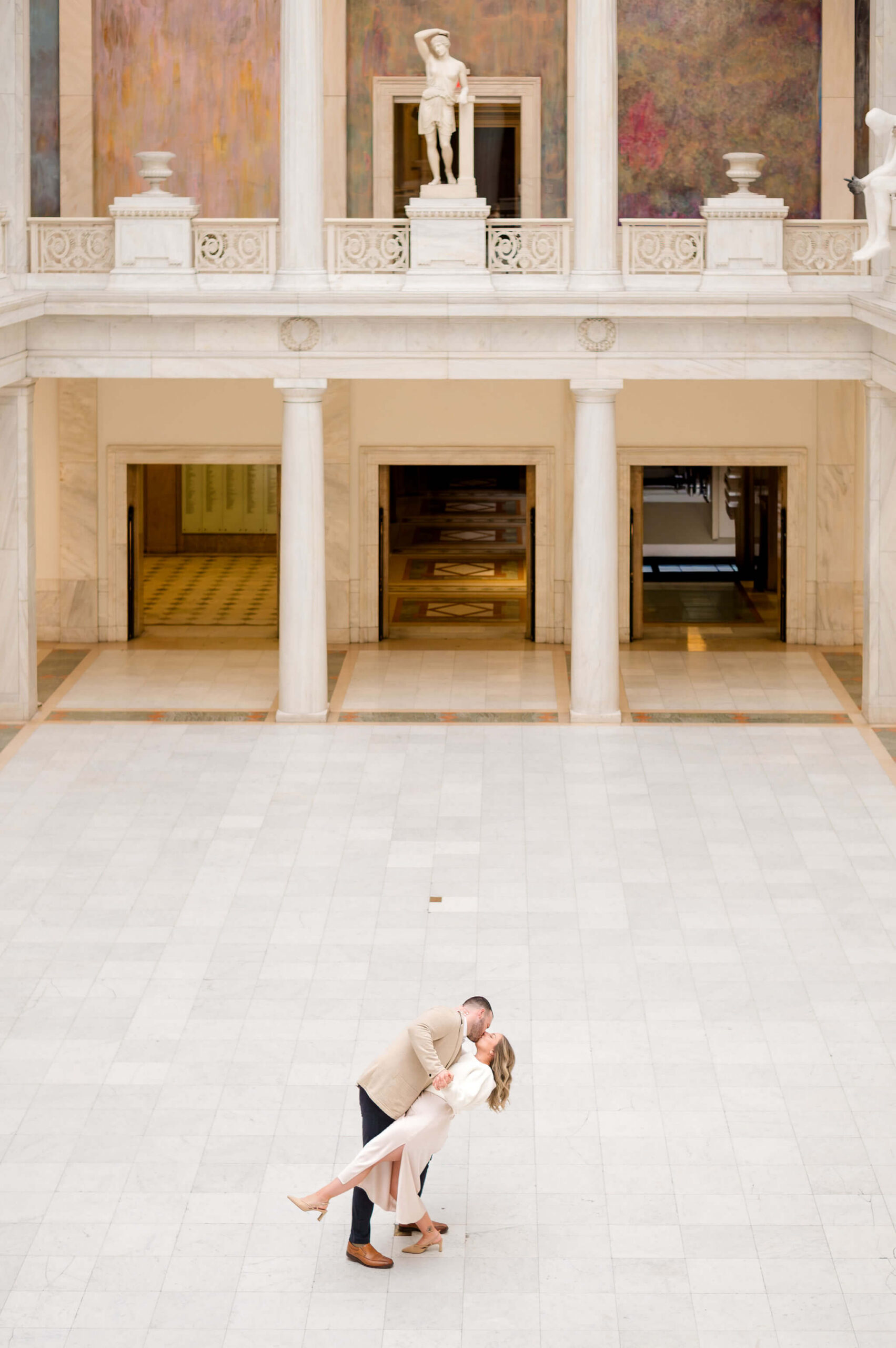 Engaged couple sharing a romantic dip and kiss on the marble floor inside the grand hall of the Carnegie Museum of Art in Pittsburgh, Pennsylvania.