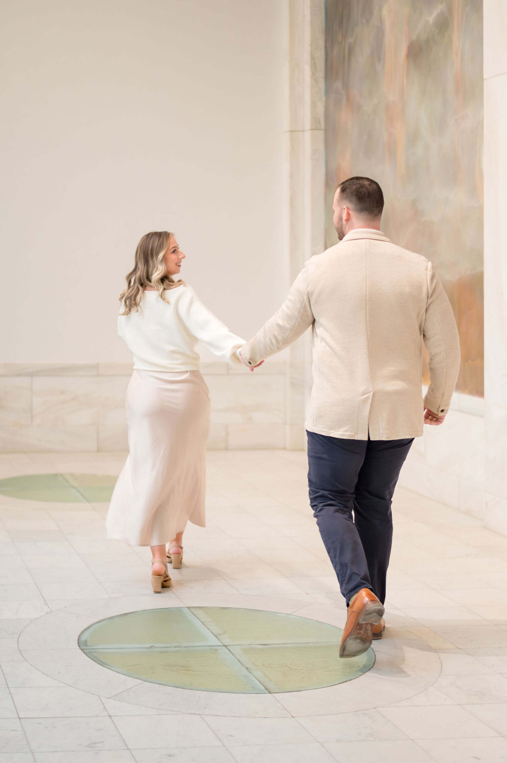 Engaged couple holding hands and walking during their bright and timeless engagement session.