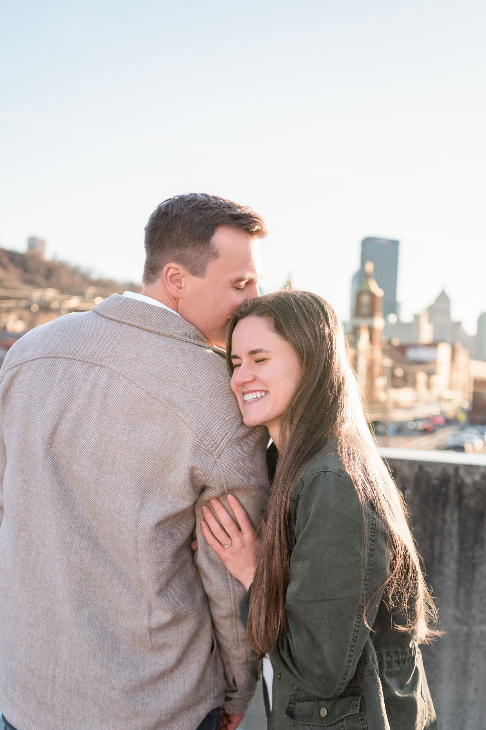 Couple sharing a warm moment together with the groom kissing the brides head while the bride faces the other way smiling. 